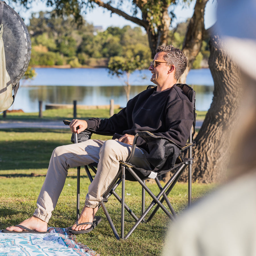 A man sitting in a camping chair by a lake.