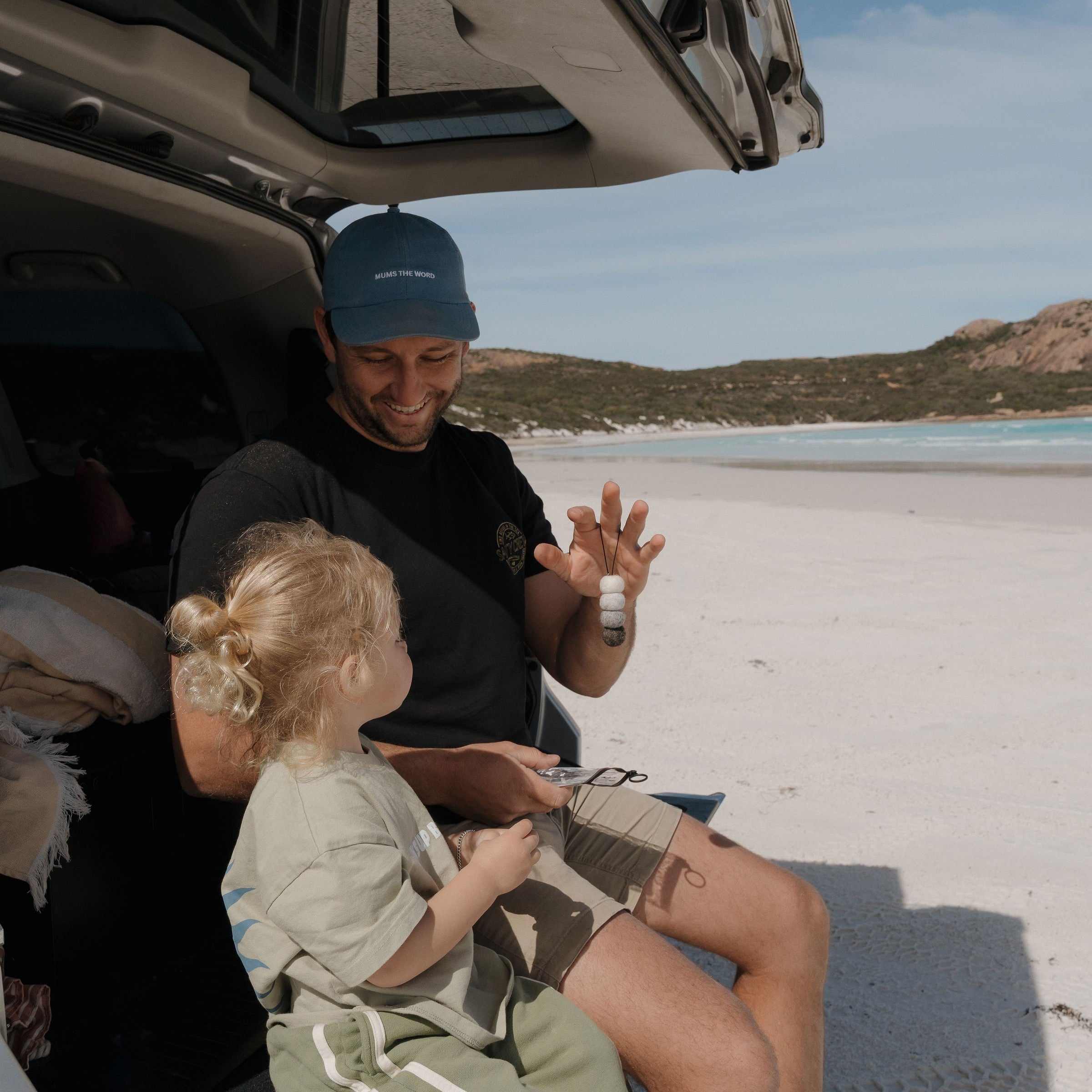 Man and child in car sitting on scenic beach in western australia with car air freshener