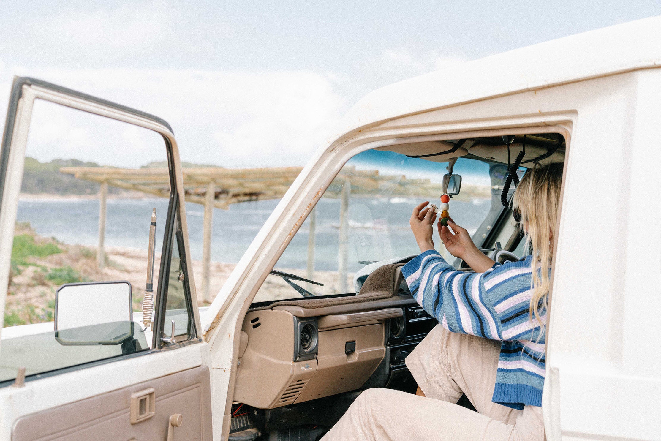 Woman in a 4WD on a coastline applying essential oil to Smelly Balls Reusable air freshener 