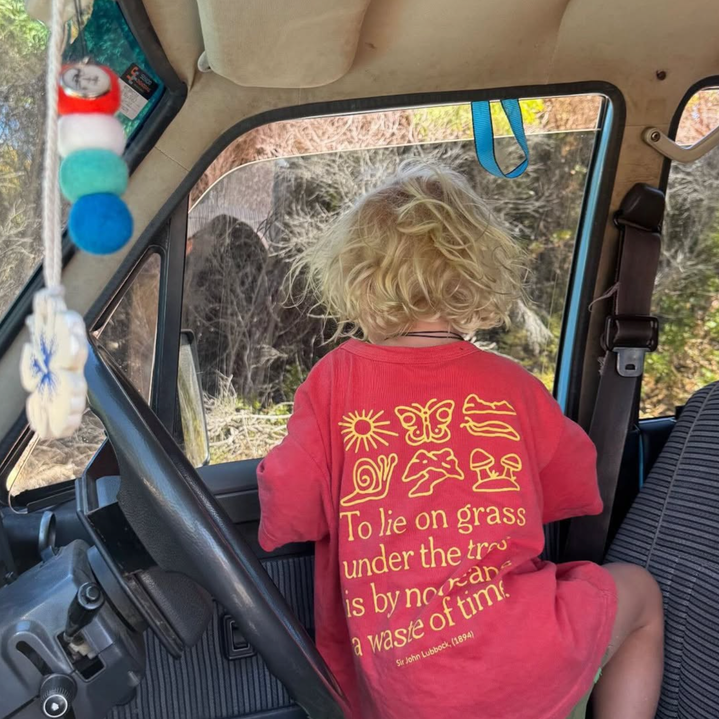Child wearing a red t-shirt with text sitting inside a vehicle.