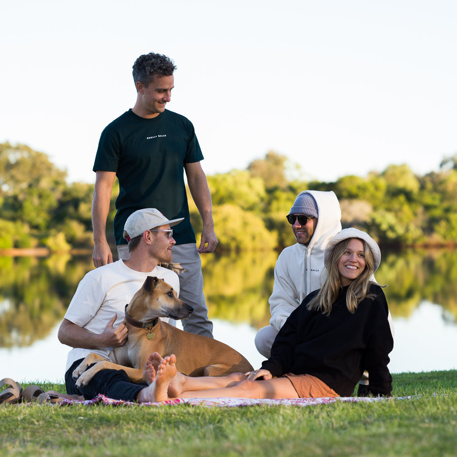 Four people and a dog sitting on grass by a lake.